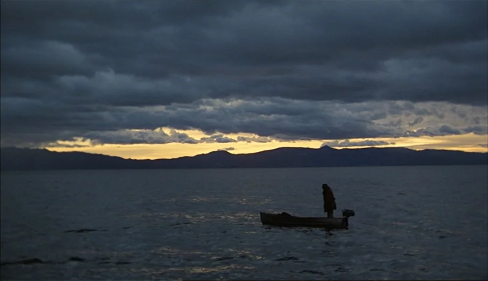 The Godfather Part II (1974) movie still: wide — A dark, expansive lake is beneath a sky filled with heavy, layered storm clouds. A lone figure…