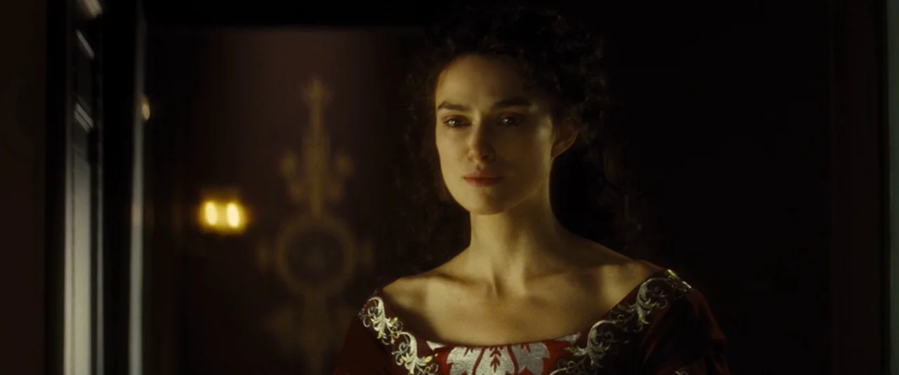 Anna Karenina (2012) movie still: medium — A dark, shadowed corridor features a wall sconce reflected in the dim background. A woman in a velvet…