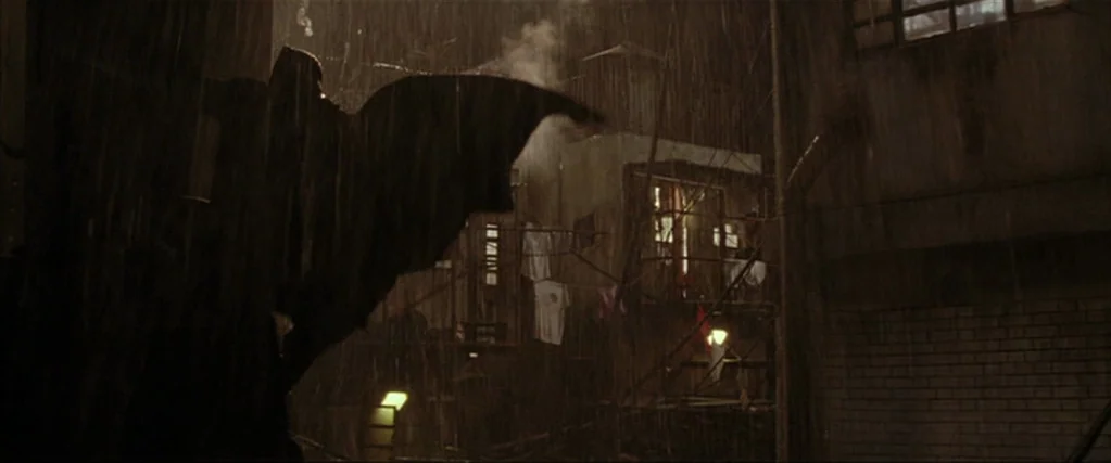 Batman Begins (2005) movie still: wide — A dense urban slum environment features dilapidated buildings with laundry hanging between rusted…