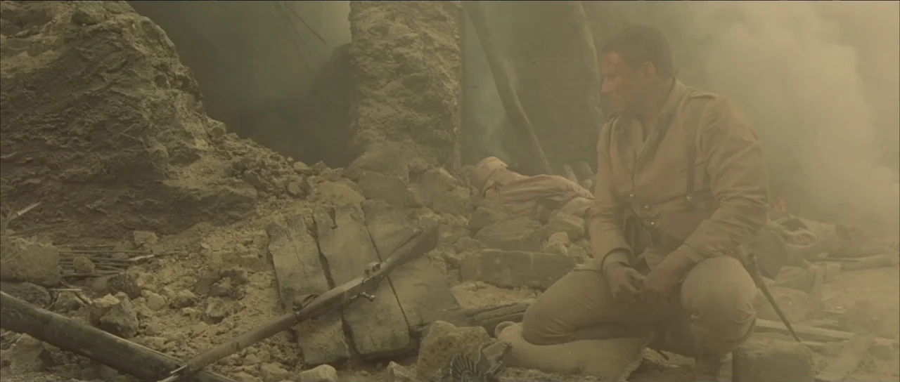 Legionario (2025) movie still: medium — A war-torn environment with crumbled stone walls and thick smoke filling the air. A lone soldier in uniform…