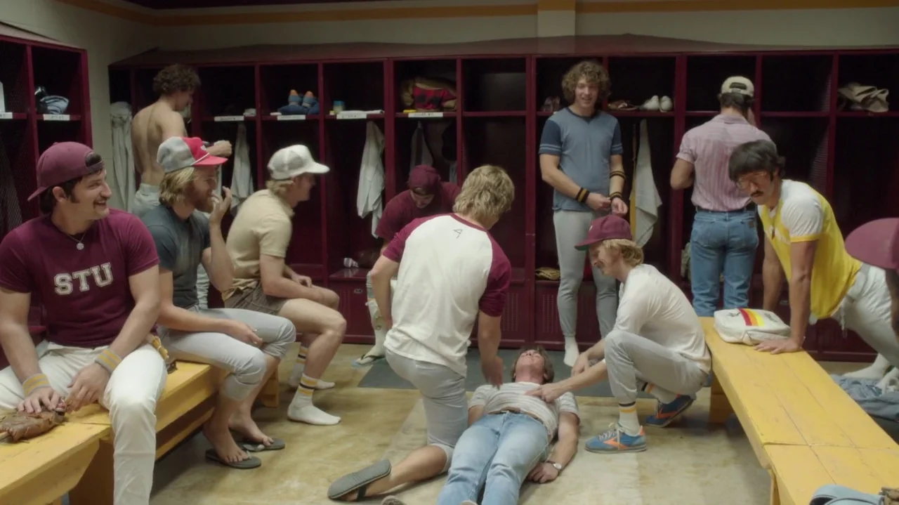 Everybody Wants Some!! (2016) movie still: fullbody — A locker room with rows of dark red wooden lockers and long yellow benches. A group of men in…
