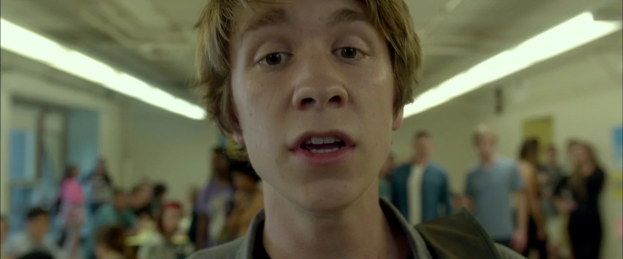 Me and Earl and the Dying Girl (2015) movie still: closeup — A crowded school hallway has students standing in the background out of focus. A young…