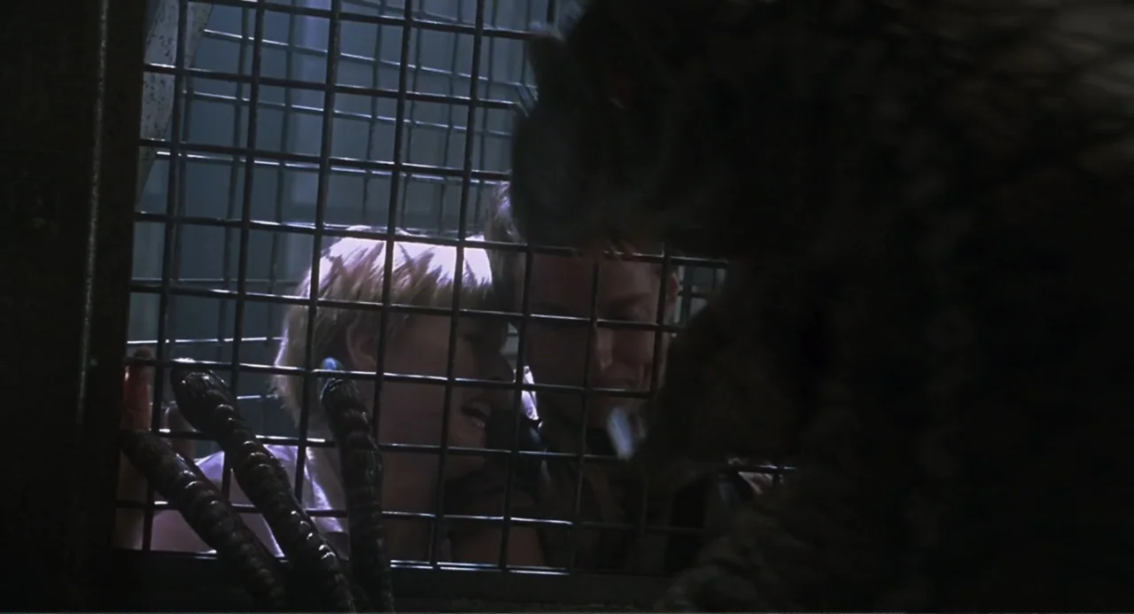 Jurassic Park III (2001) movie still: medium — A dark, industrial-looking confinement space features heavy black iron bars forming a protective…