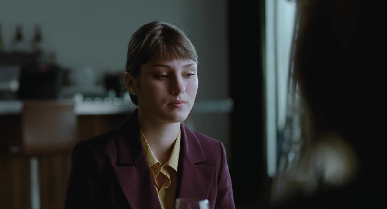 The Worst Person in the World (2021) movie still: medium — A dimly lit indoor space with modern furnishings and a dark background. A young woman…