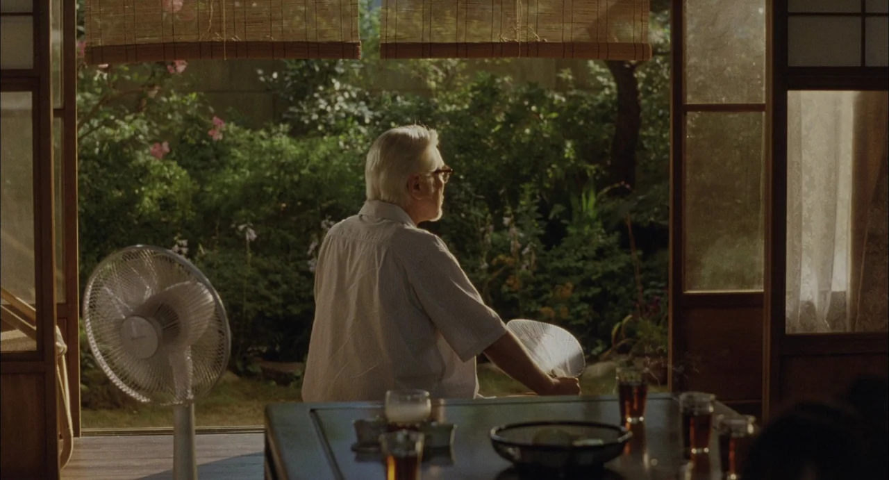 Still Walking (2008) movie still: medium — A traditional Japanese room opens to a lush garden through wooden sliding doors. An elderly man sits at a…