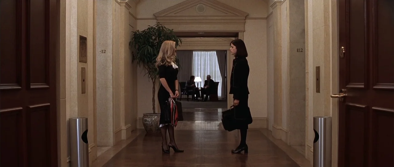 Legally Blonde (2001) movie still: fullbody — A quiet hotel corridor features light-colored walls, patterned floors, and two stainless steel trash…