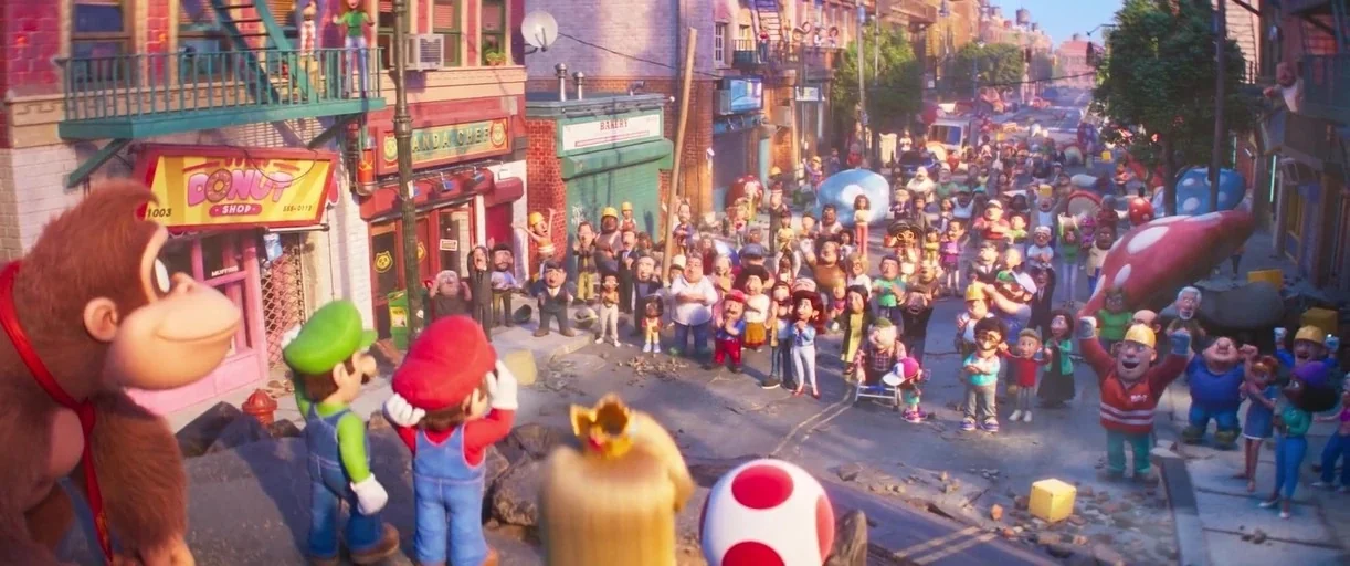The Super Mario Bros. Movie (2023) movie still: wide — A stylized city street features brick storefronts and a crowd of onlookers standing together.…