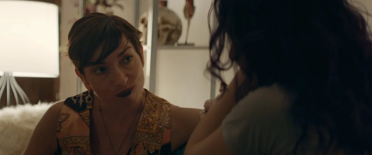 Mennonite's Bite (2023) movie still: medium — A dimly lit room contains shelving units holding a decorative skull and other objects. A woman with…