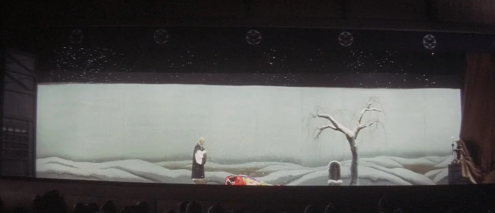 An Actor’s Revenge (1963) movie still: wide — A theatrical stage features a wide painted backdrop of a snowy, desolate landscape. A performer in…