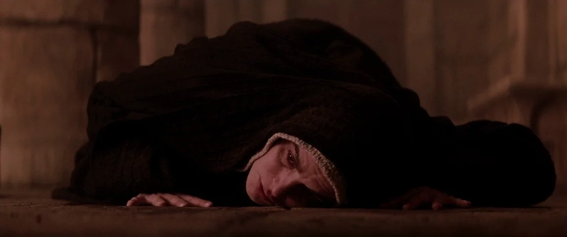The Passion of the Christ (2004) movie still: medium — A dark, stone-floored interior with structural pillars visible in the dim background. A woman…