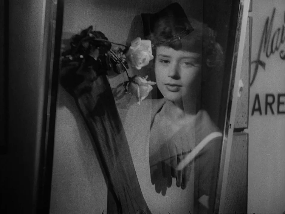 Dreams (1955) movie still: medium — A woman looks through a storefront window with a display of white roses. Superimposed reflections of the store…