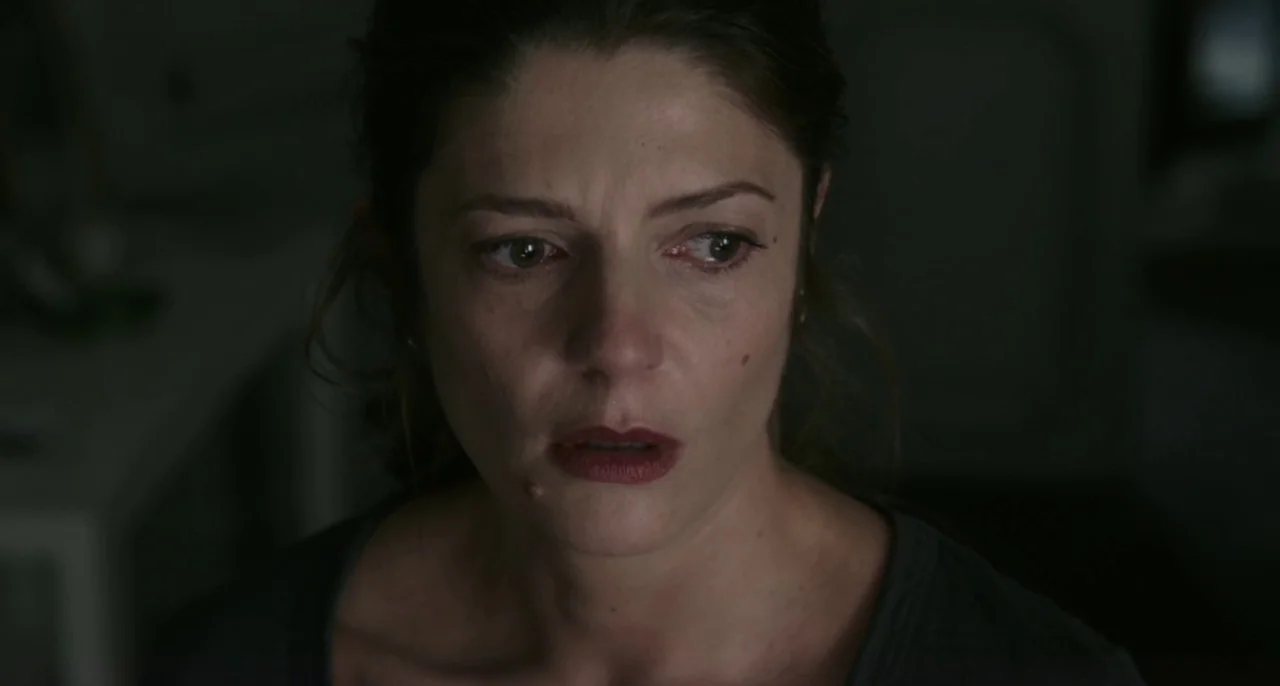 Bastards (2013) movie still: closeup — A dimly lit room provides a dark background for the subject in close-up. A woman in a grey t-shirt looks…