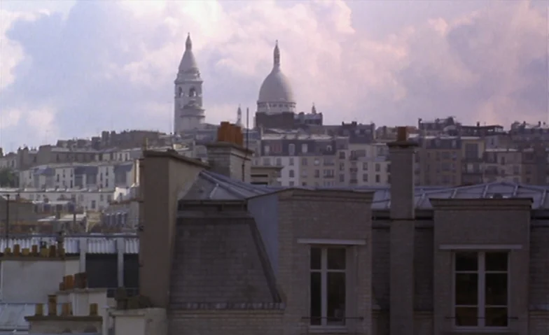 I Can’t Sleep (1994) movie still: establishing — An urban cityscape with a prominent white stone cathedral dome rising above residential buildings.…