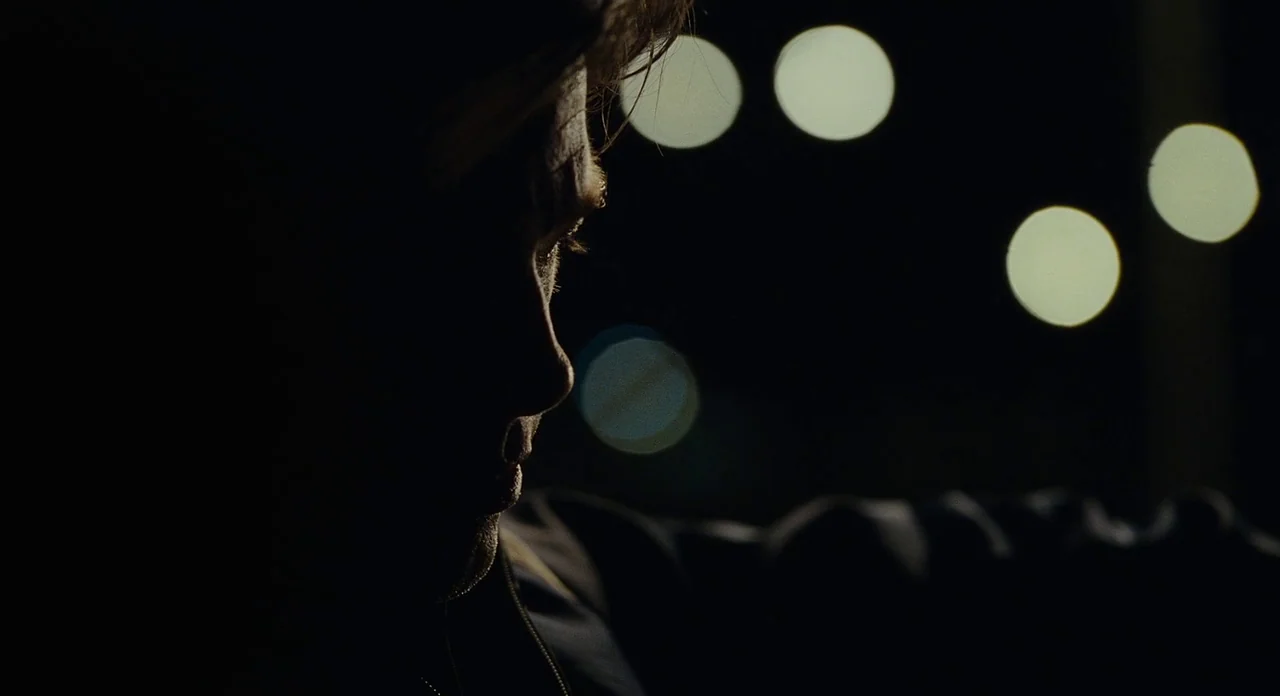 Moneyball (2011) movie still: closeup — A dark, blurred city environment provides the background for this close-up frame. A man's face is partially…