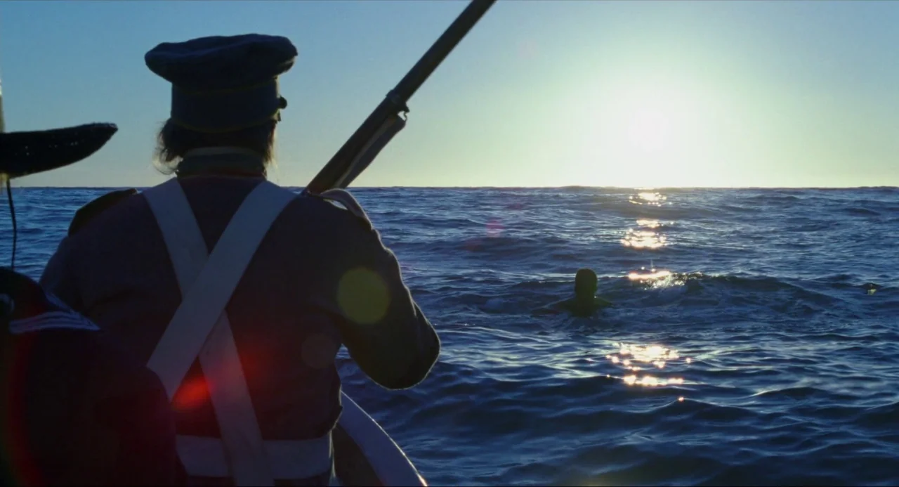 Amistad (1997) movie still: medium — The open ocean reflects bright sunlight under a clear sky during the day. A soldier in a military uniform sits…