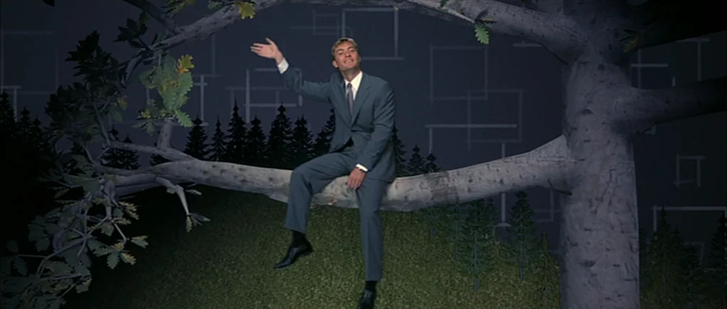 I Heart Huckabees (2004) movie still: fullbody — A theatrical studio set features a painted backdrop of geometric shapes and stylized pine trees. A…