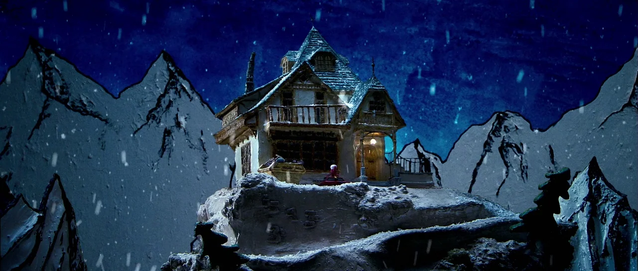 Bunny and the Bull (2009) movie still: wide — A miniature wooden cabin with a gabled roof sits atop a snowy mountain peak. White snow falls against…