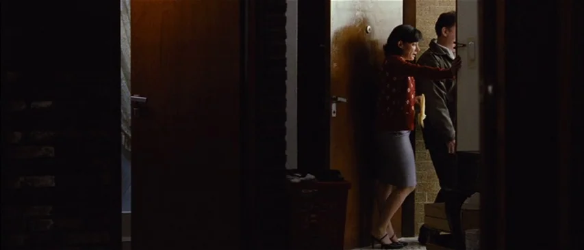 The Headless Woman (2008) movie still: medium — A dimly lit narrow apartment hallway features dark wooden doors and textured wall surfaces. A woman…