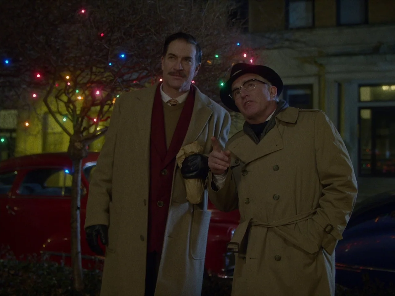 Brooklyn 45 (2023) movie still: medium — Two men stand on a dark residential street illuminated by scattered multi-colored holiday lights. One man…