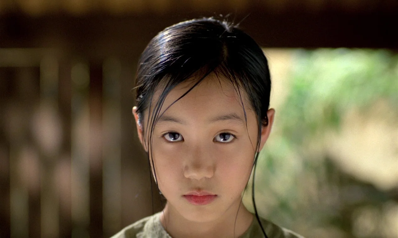 The Scent of Green Papaya (1993) movie still: closeup — An east asian child stands outdoors against a background of foliage and trees. The child…