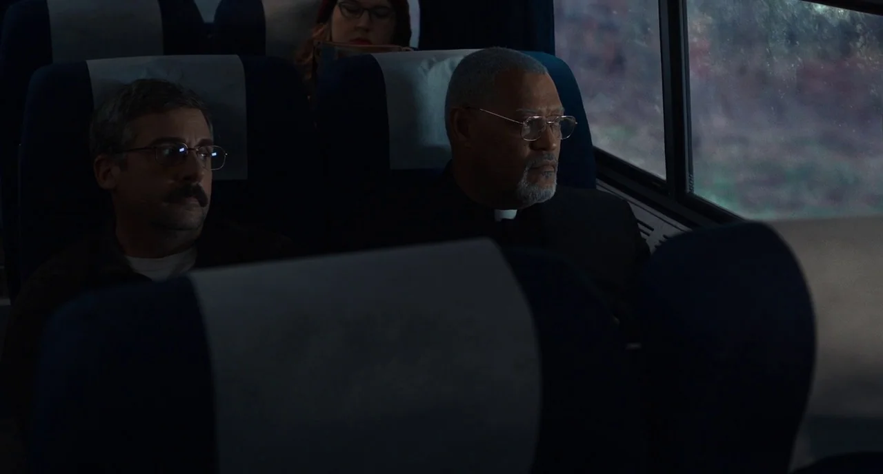 Last Flag Flying (2017) movie still: medium — The interior of a bus with rows of blue and grey padded seats. Two men in glasses sit in adjacent…