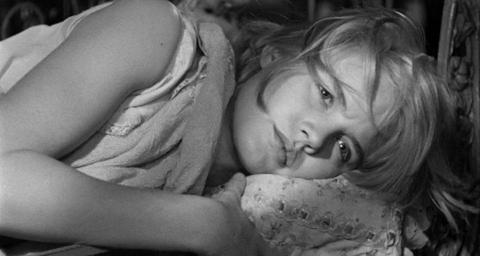 Baby Doll (1956) movie still: closeup — A dimly lit bedroom features a woman resting her head on a patterned pillow. She lies on her side, facing…