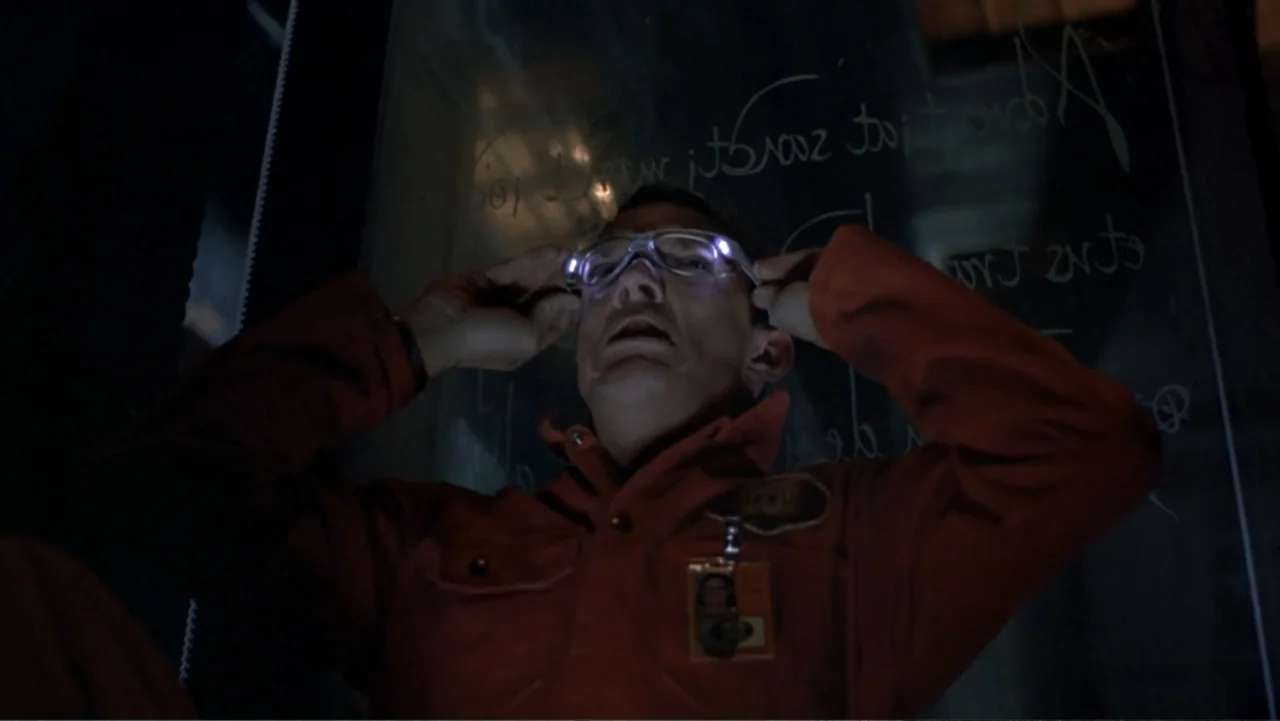 13 Ghosts (1960) movie still: medium — A man sits before a glass pane with handwritten text in a dark workspace. He adjusts clear protective glasses…