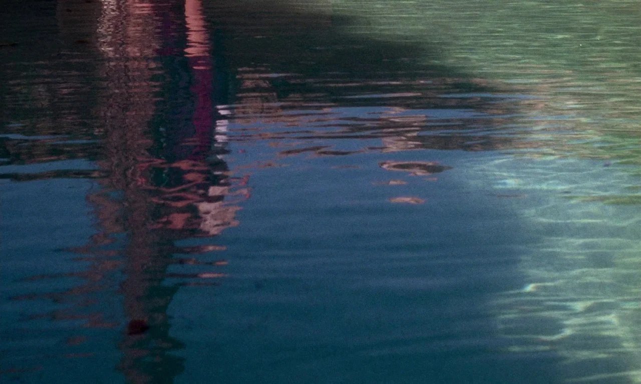 The Margin (1976) movie still: establishing — The surface of dark water displays ripples and a distorted reflection of colors. Sunlight creates…