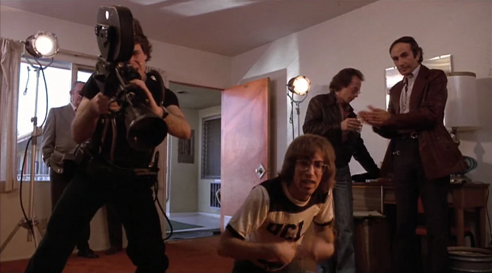 Hardcore (1979) movie still: medium — A 1970s motel room with orange carpeting and basic furniture pieces. A film crew captures a scene as a man in…