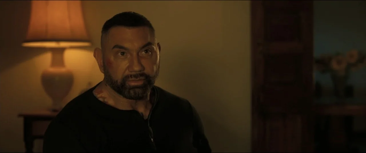 My Spy The Eternal City (2024) movie still: medium — A dimly lit room features a table lamp glowing in the blurred background. A large muscular man…