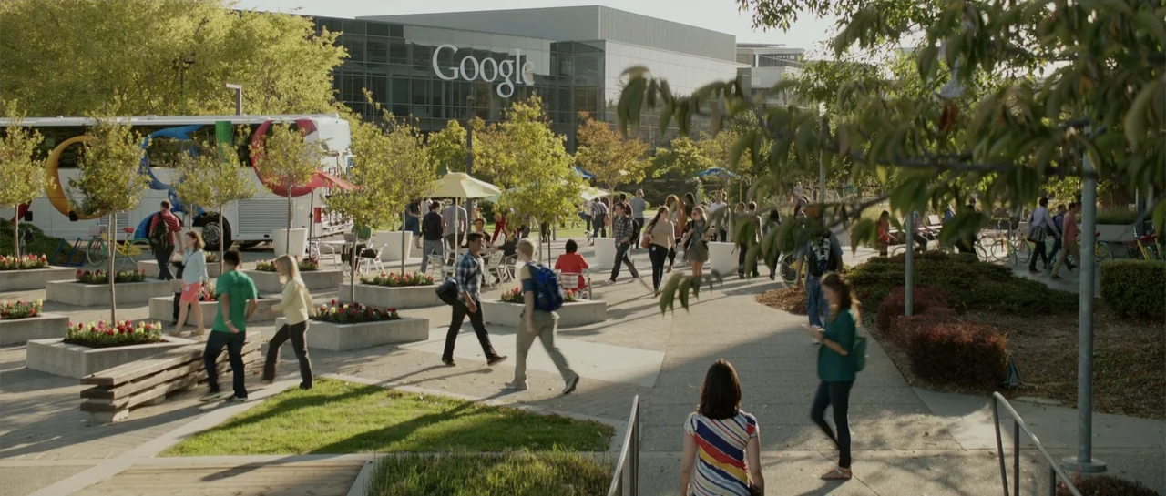 The Internship (2013) movie still: wide — A sunny outdoor campus features concrete planters with flowers and numerous pedestrian walkways. Various…