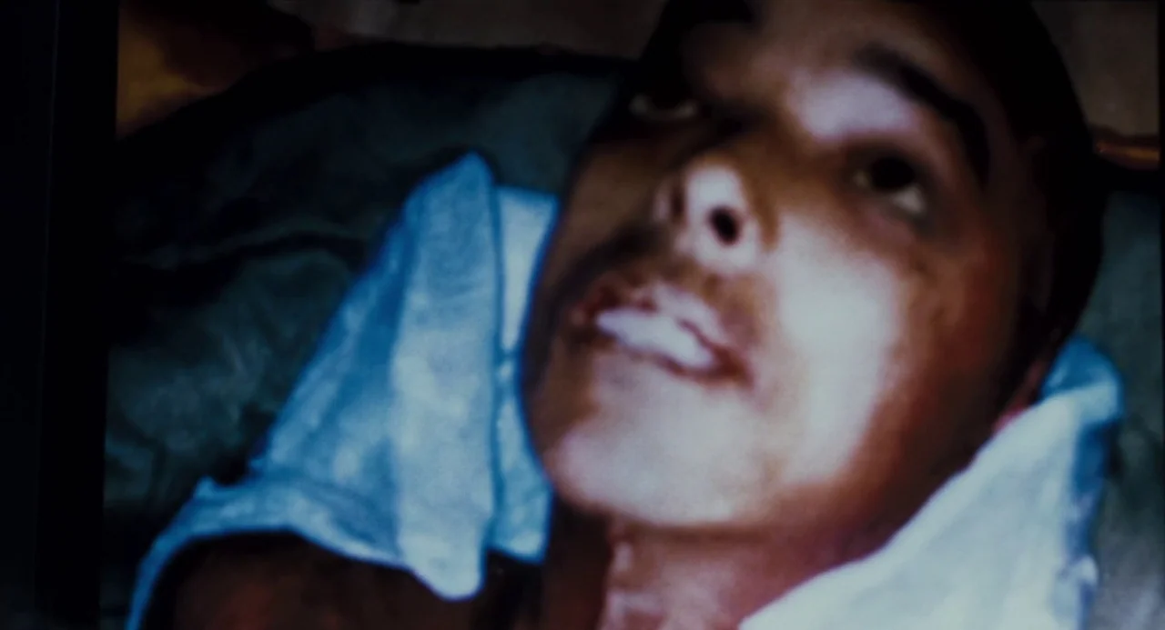 Martyrs (2008) movie still: closeup — A man lies on white sheets within a dimly lit interior space. He gazes upward with his mouth slightly open.
