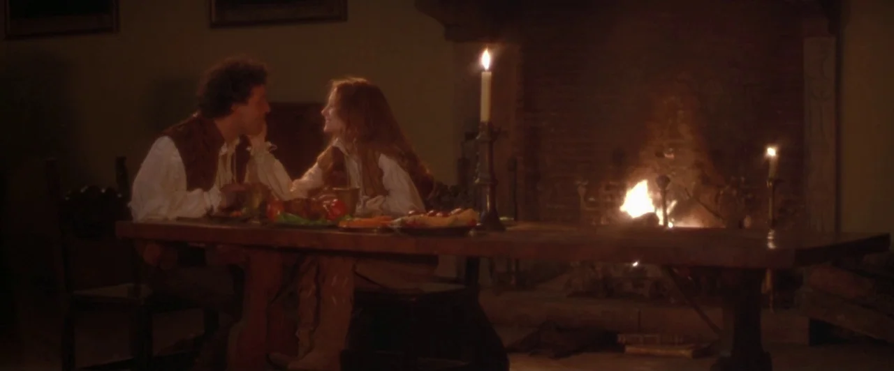 Dangerous Beauty (1998) movie still: medium — A dimly lit room features a large heavy wooden dining table near a stone hearth. A man and a woman sit…