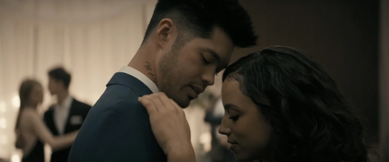 Perfect Addiction (2023) movie still: medium — A dimly lit ballroom interior features a couple dancing close together in the foreground. They rest…