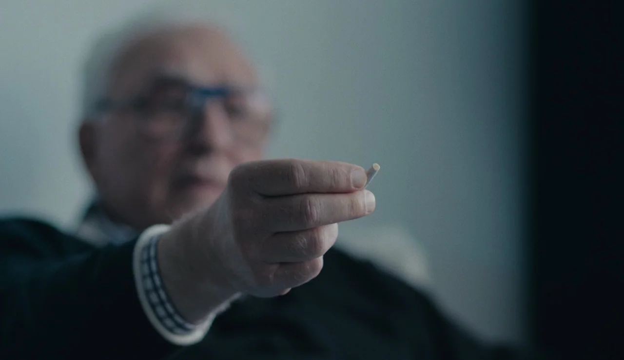 Land Ho! (2014) movie still: closeup — A dimly lit indoor space with neutral-toned walls provides the backdrop for the subject. An elderly man holds…