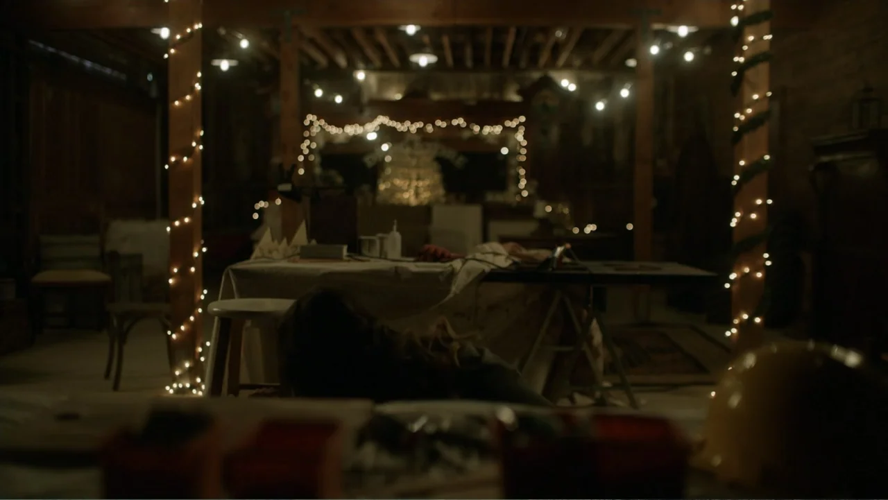 A Carpenter Christmas Romance (2024) movie still: medium — A dimly lit wooden workshop space features a central table draped in white fabric. A…