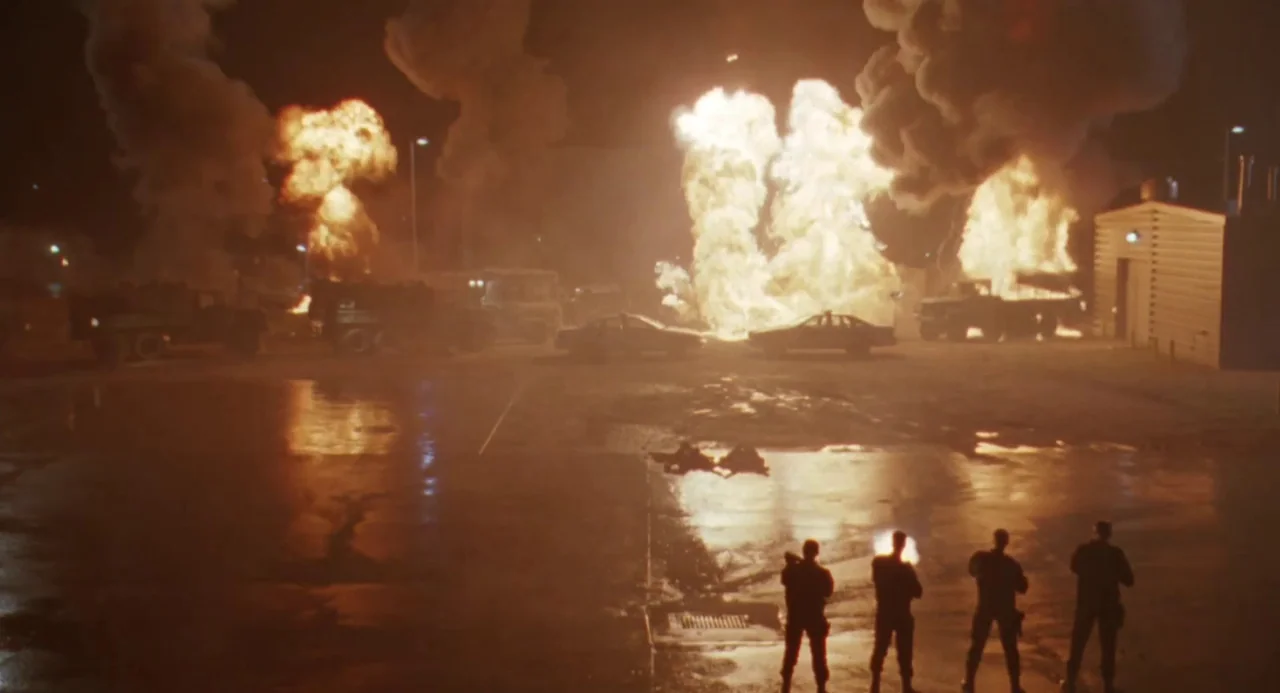 Universal Soldier: The Return (1999) movie still: wide — A dark, wet asphalt parking lot is filled with towering plumes of fire and smoke. Four…