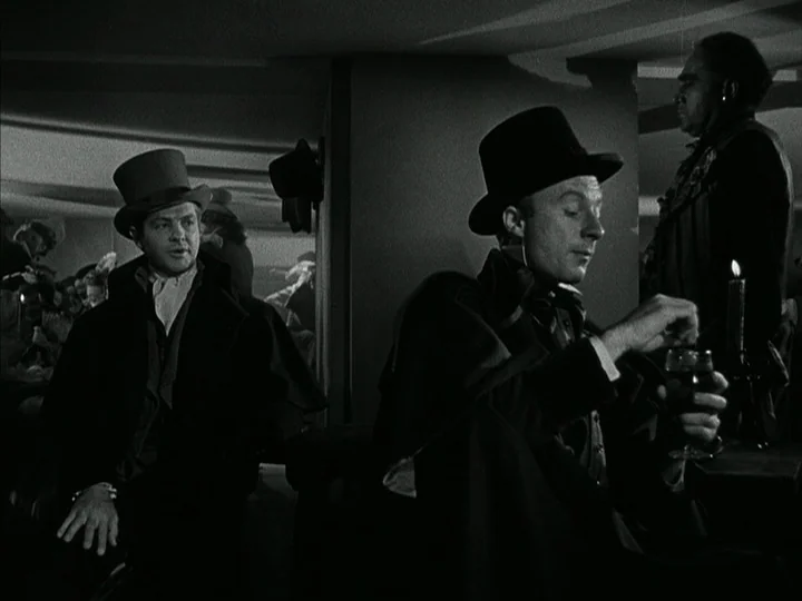 The Black Book (Reign of Terror) (1949) movie still: medium — A dimly lit 19th-century-style tavern interior featuring men in formal capes and top…