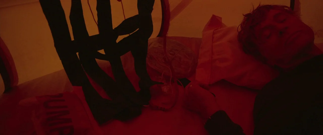 All Is Lost (2013) movie still: closeup — A person lies on a white pillow in a dark, red-lit medical space. A black strap harness sits on the…