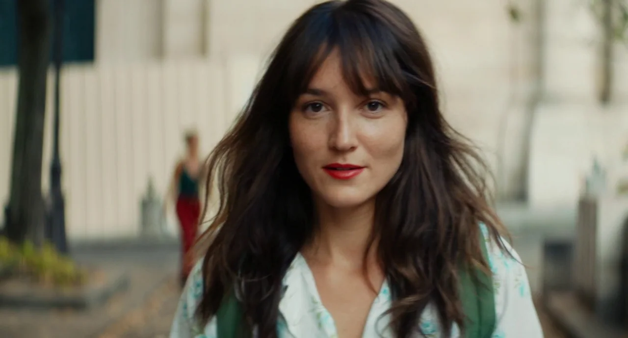 Anaïs in Love (2021) movie still: closeup — A woman walks down a city street lined with neutral-toned buildings. The woman moves towards the camera…