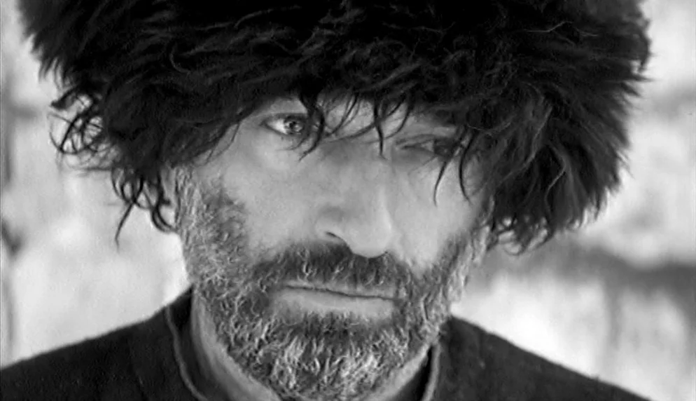 The Plea (1968) movie still: closeup — A man with a thick fur hat stands against a bright, out-of-focus background. The man gazes toward the side of…