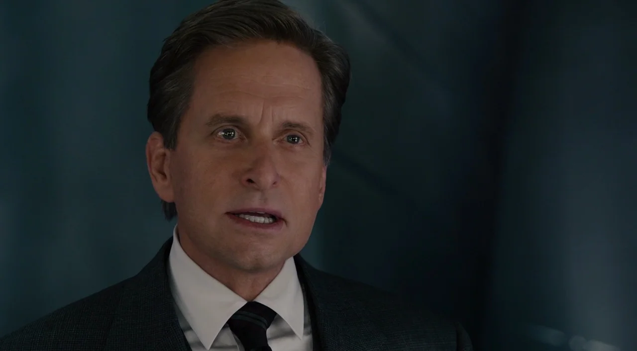 Ant-Man (2015) movie still: closeup — A dimly lit room with a dark wall surface visible behind the man. The man is talking while looking toward the…