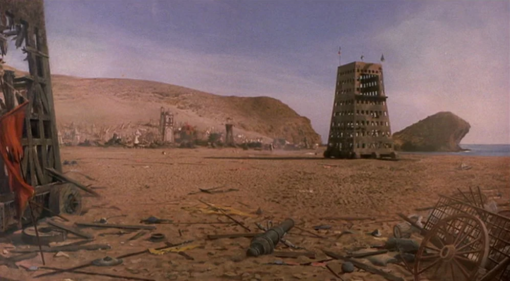 The Adventures Of Baron Munchausen (1988) movie still: establishing — A wide, deserted beach is covered in scattered weapons, broken carts, and…