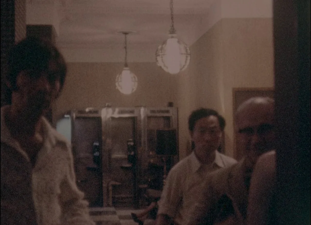 Hotel Monterey (1973) movie still: medium — A dimly lit hotel lobby features metallic phone booths in the background. Three men stand in the…