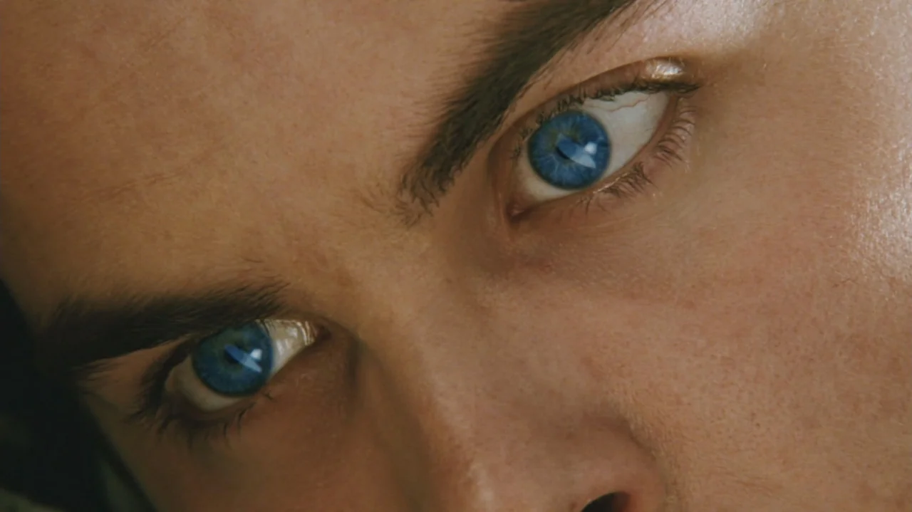 Zoom (2006) movie still: closeup — A person's face fills the frame in a tight close-up shot. The person's bright blue eyes look directly into the…