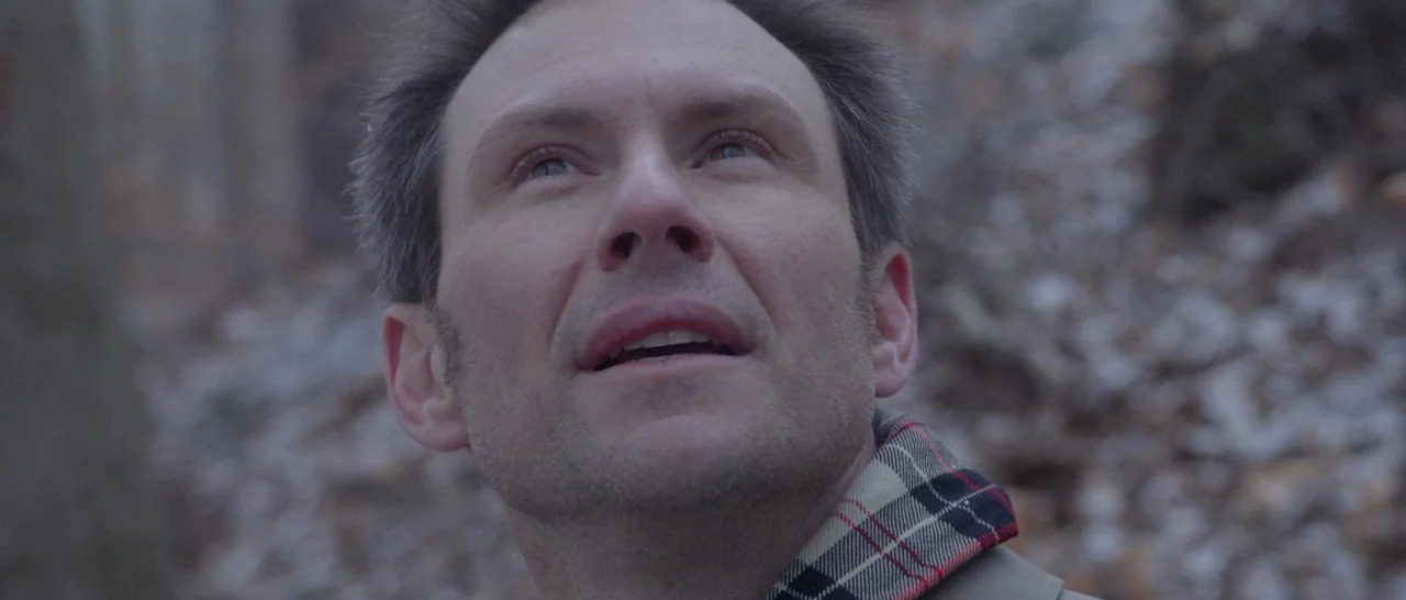 Nymphomaniac Vol 2 (2013) movie still: closeup — A dense woodland with dry, fallen leaves scattered across the ground. A middle-aged man looks…