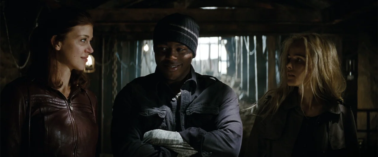 Red Dawn (2012) movie still: medium — A dark attic contains wooden beams and hanging ropes in the blurred background. Two women and one man stand in…