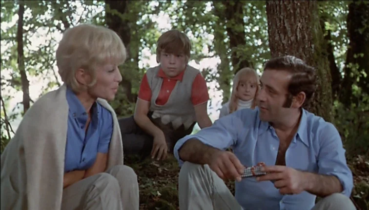 Le Boucher (1970) movie still: medium — A group of four people sit on the ground amidst trees in a wooded area. The adults engage in conversation…