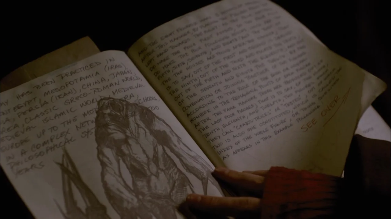 Silent Hill: Revelation 3D (2012) movie still: closeup — An open vintage book rests on a surface with handwritten notes and a sketch. Two hands hold…