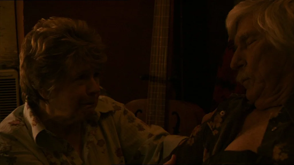 A Prairie Home Companion movie still: medium — A dark indoor space with a guitar standing vertically in the background shadow. An elderly woman…